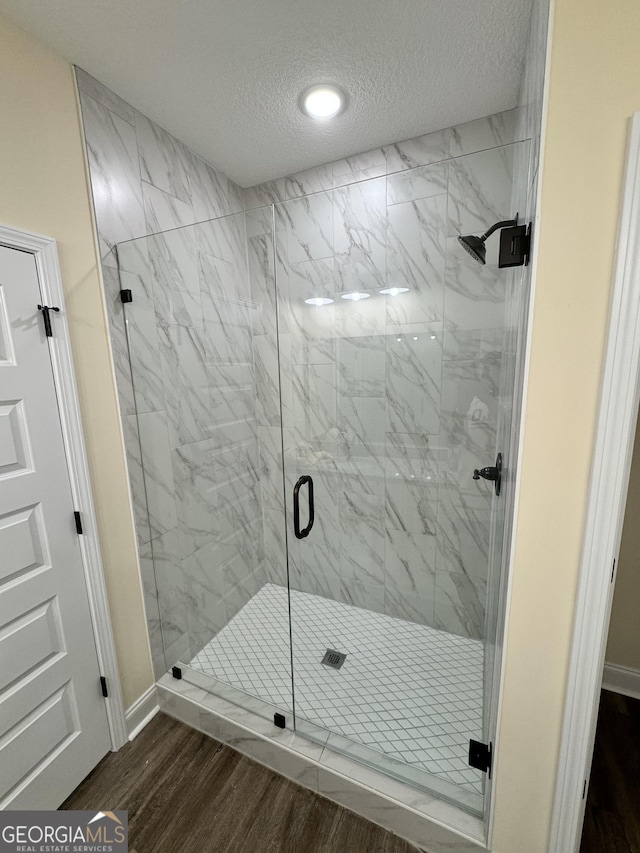 bathroom featuring wood-type flooring, a shower with door, and a textured ceiling