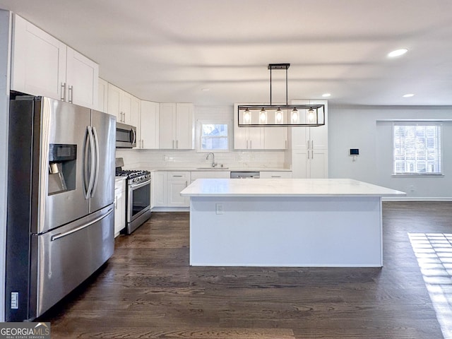 kitchen featuring decorative light fixtures, white cabinetry, a center island, stainless steel appliances, and dark wood-type flooring