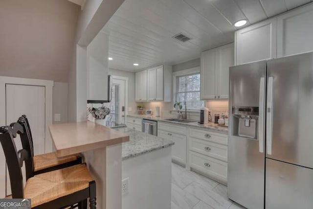 kitchen featuring sink, light stone counters, appliances with stainless steel finishes, a kitchen breakfast bar, and white cabinets