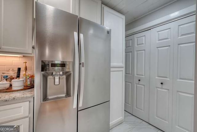 kitchen with white cabinetry, stainless steel refrigerator with ice dispenser, light stone countertops, and decorative backsplash