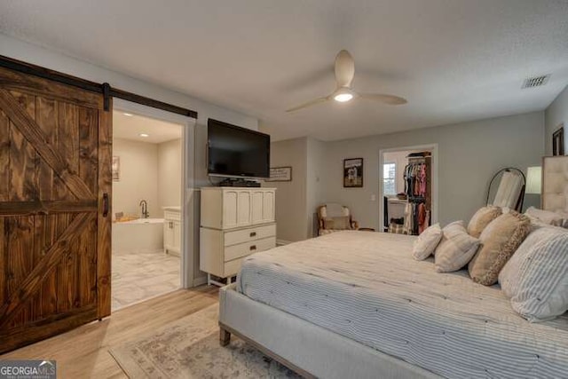 bedroom featuring connected bathroom, a walk in closet, a barn door, light wood-type flooring, and a closet