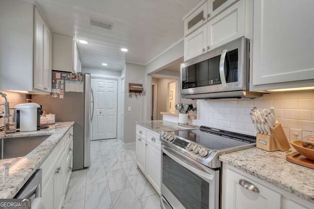 kitchen with sink, appliances with stainless steel finishes, backsplash, light stone countertops, and white cabinets