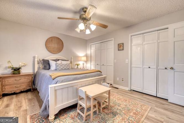 bedroom featuring ceiling fan, two closets, light hardwood / wood-style flooring, and a textured ceiling