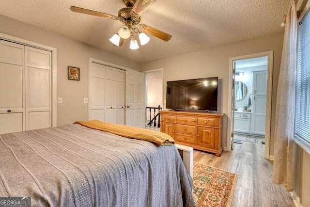 bedroom featuring ceiling fan, a textured ceiling, light hardwood / wood-style flooring, and two closets