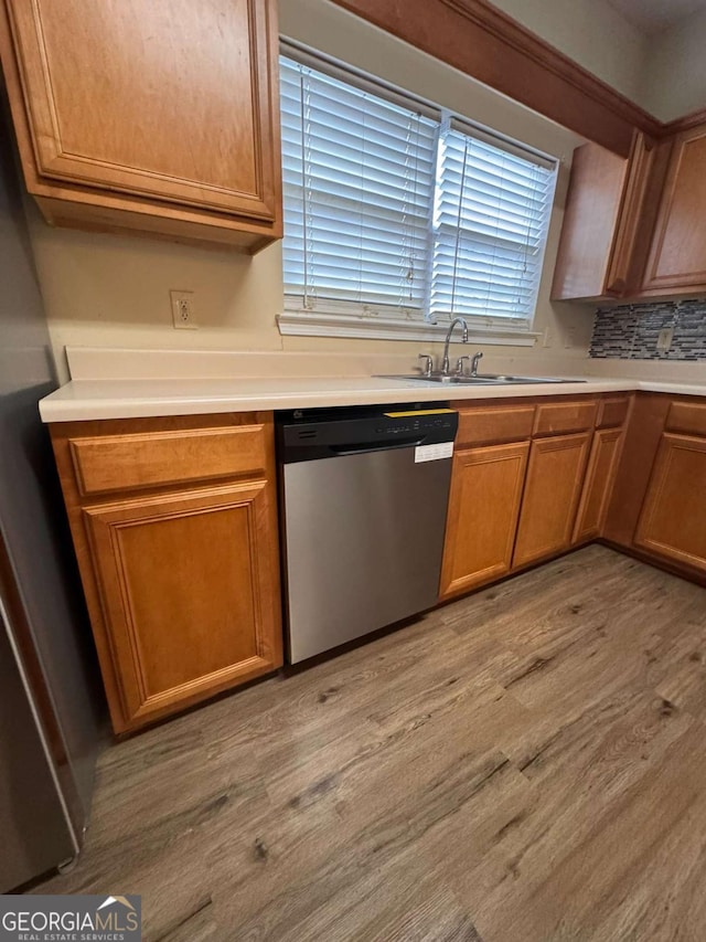 kitchen with sink, decorative backsplash, stainless steel dishwasher, and light wood-type flooring