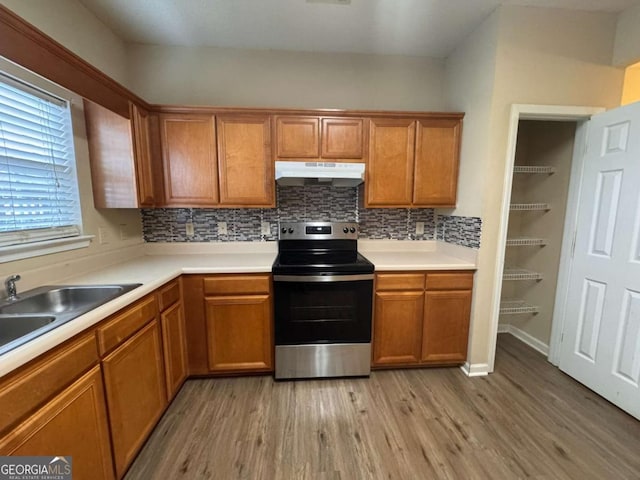 kitchen featuring stainless steel range with electric stovetop, backsplash, light hardwood / wood-style floors, and sink