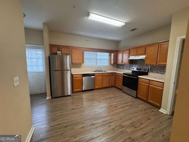 kitchen featuring sink, tasteful backsplash, a textured ceiling, appliances with stainless steel finishes, and light hardwood / wood-style floors