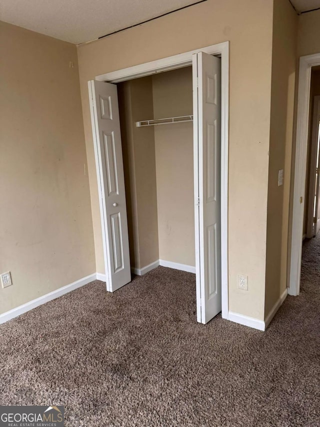 unfurnished bedroom featuring dark carpet and a closet