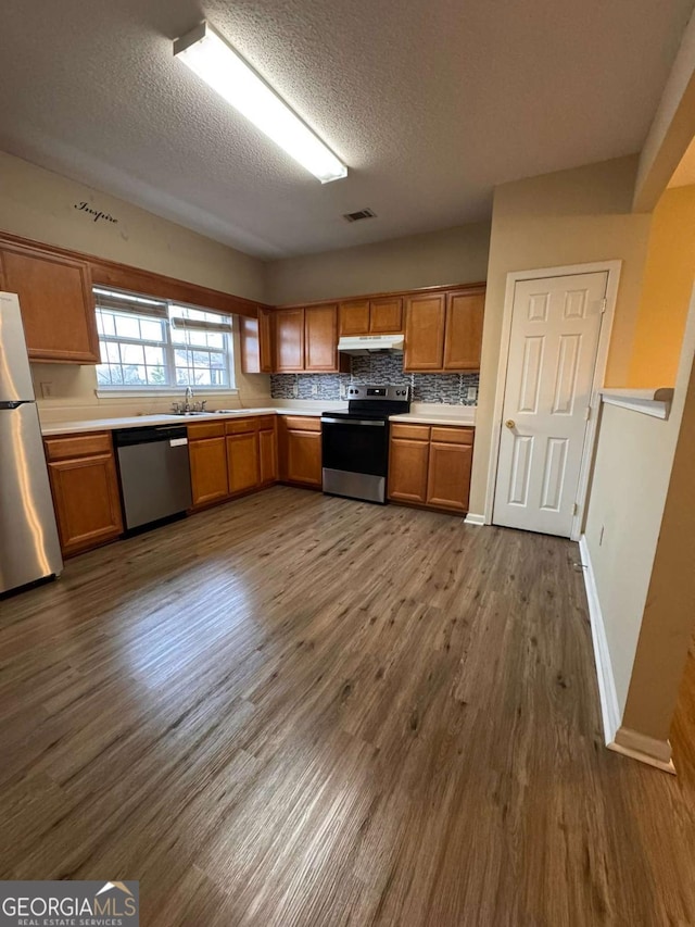 kitchen featuring sink, a textured ceiling, hardwood / wood-style flooring, stainless steel appliances, and decorative backsplash