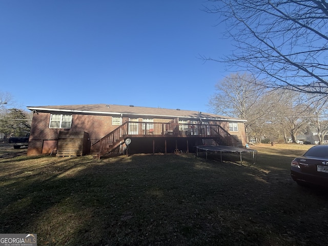 back of property with a wooden deck, a yard, and a trampoline