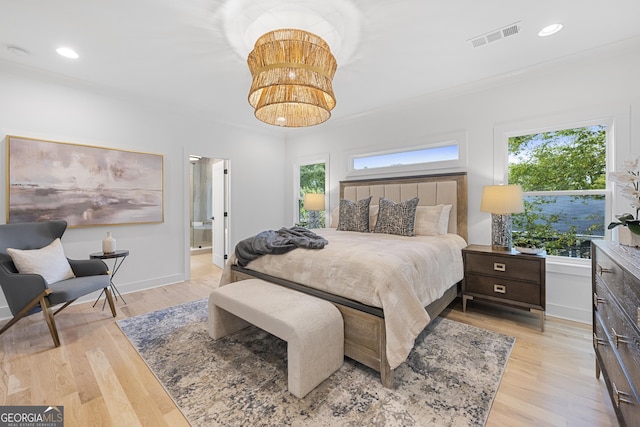 bedroom with an inviting chandelier, ornamental molding, light hardwood / wood-style floors, and ensuite bathroom