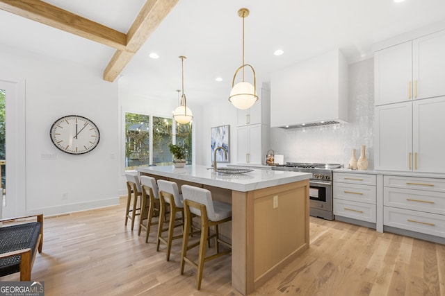 kitchen featuring a center island with sink, white cabinetry, wall chimney range hood, and high end stove