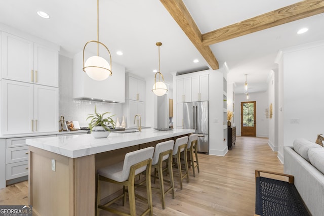 kitchen featuring high end fridge, white cabinetry, a kitchen island with sink, and decorative light fixtures