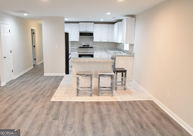 kitchen featuring freestanding refrigerator, electric stove, exhaust hood, white cabinets, and a sink