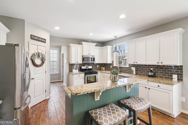 kitchen with a breakfast bar area, plenty of natural light, pendant lighting, stainless steel appliances, and white cabinets