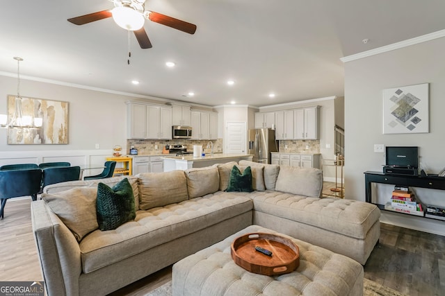 living room with ornamental molding, ceiling fan with notable chandelier, and light hardwood / wood-style floors