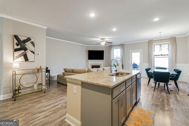 kitchen featuring sink, crown molding, light hardwood / wood-style flooring, an island with sink, and light stone countertops