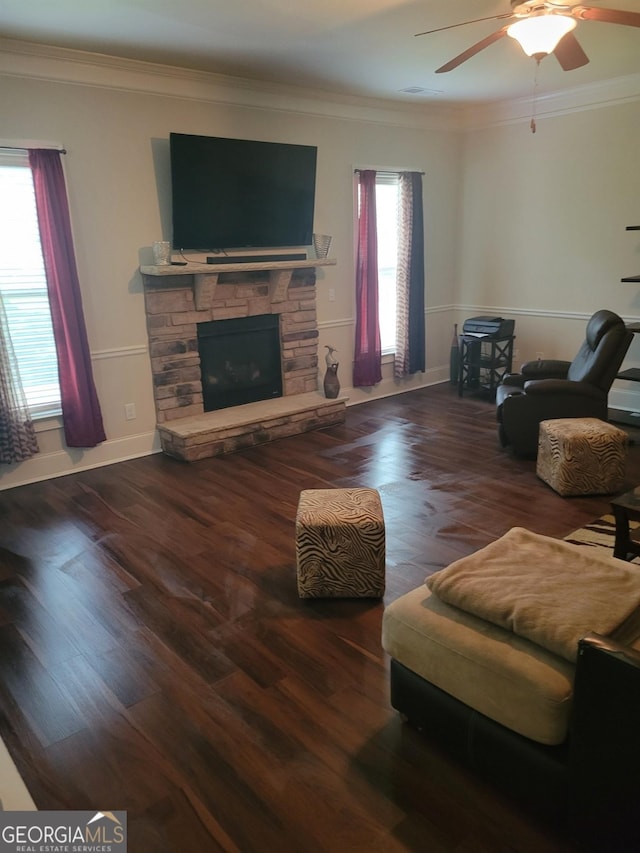 living room featuring ornamental molding, a stone fireplace, hardwood / wood-style floors, and ceiling fan