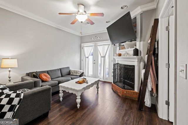 living area with a fireplace with raised hearth, ornamental molding, french doors, wood finished floors, and a ceiling fan