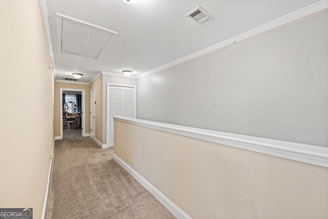 hallway featuring visible vents, carpet, crown molding, baseboards, and attic access