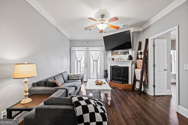 living room with a brick fireplace, crown molding, dark wood-type flooring, and ceiling fan