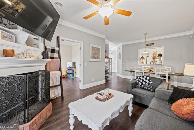 living area featuring a ceiling fan, baseboards, a fireplace with raised hearth, dark wood-style flooring, and ornamental molding