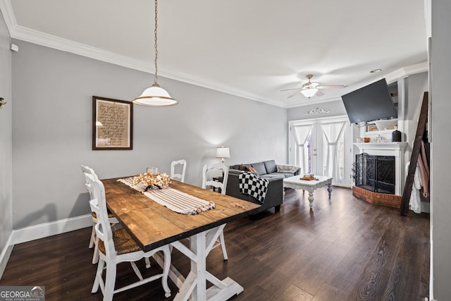 dining room featuring wood finished floors, a fireplace, crown molding, baseboards, and ceiling fan