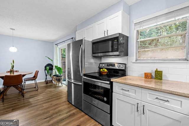 kitchen featuring white cabinetry, light stone counters, hanging light fixtures, appliances with stainless steel finishes, and dark hardwood / wood-style flooring