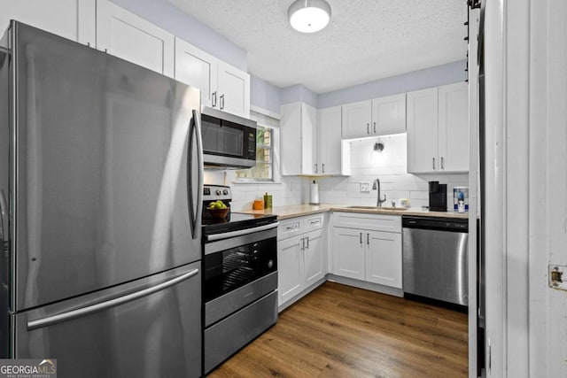 kitchen with appliances with stainless steel finishes, sink, dark wood-type flooring, and white cabinets