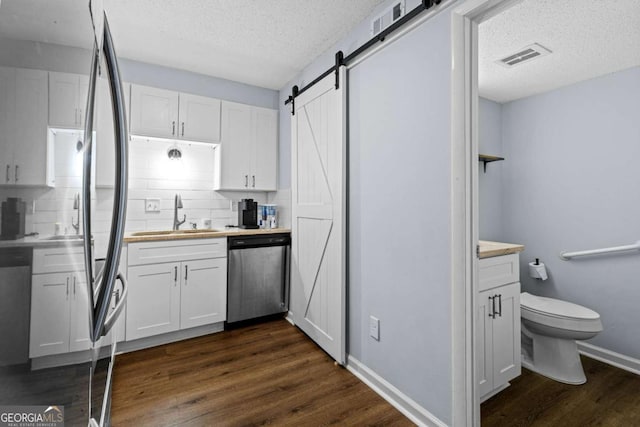 kitchen with sink, dark hardwood / wood-style floors, dishwasher, a barn door, and white cabinets