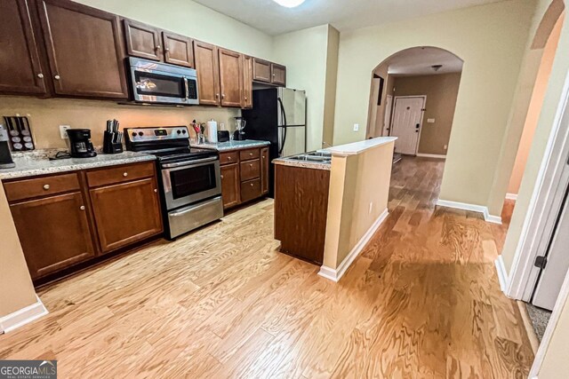 kitchen with stainless steel appliances, light stone countertops, dark brown cabinetry, and light hardwood / wood-style flooring