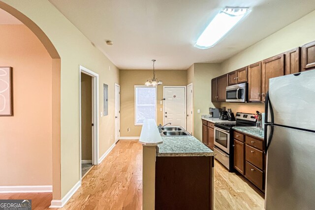 kitchen with sink, appliances with stainless steel finishes, hanging light fixtures, light hardwood / wood-style floors, and a center island with sink