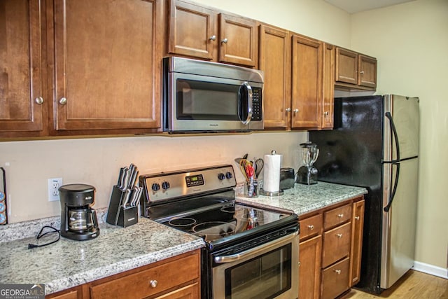 kitchen with light stone countertops, appliances with stainless steel finishes, and light wood-type flooring