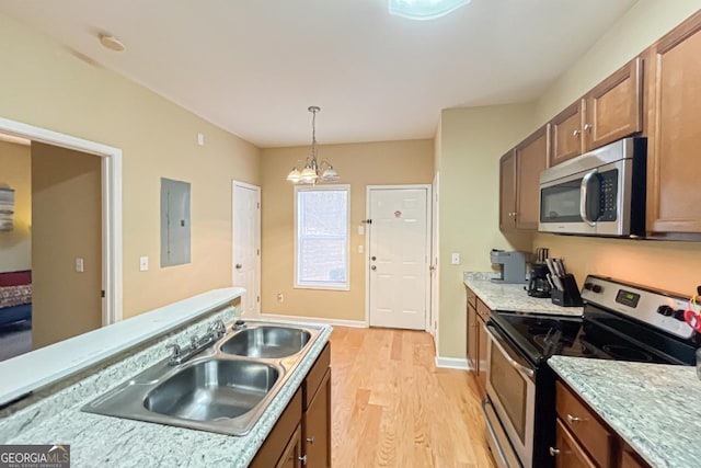 kitchen featuring decorative light fixtures, sink, electric panel, stainless steel appliances, and light wood-type flooring