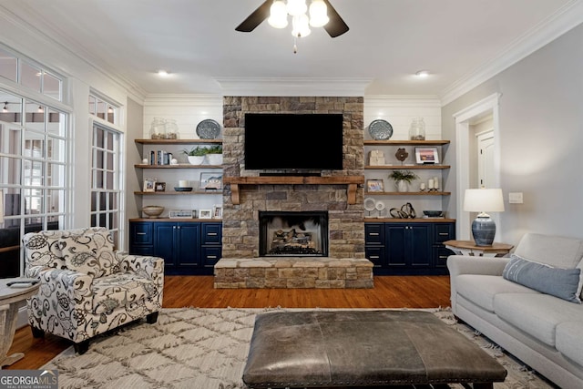 living room with dark wood-type flooring, ceiling fan, ornamental molding, and a stone fireplace