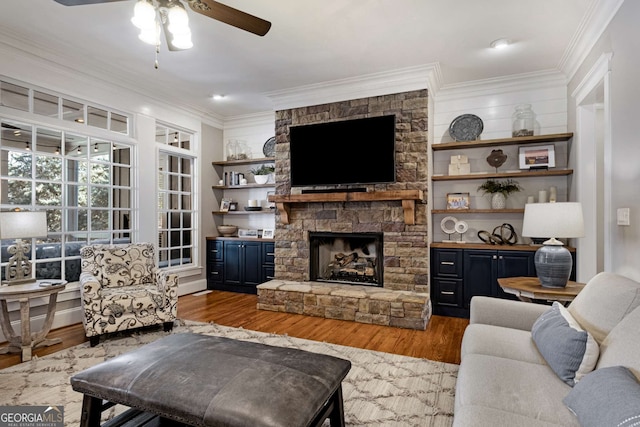 living room featuring ceiling fan, ornamental molding, a fireplace, and light hardwood / wood-style flooring