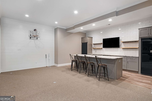 kitchen featuring gray cabinetry, light colored carpet, an island with sink, and a breakfast bar