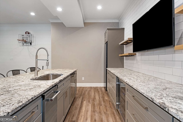 kitchen with sink, gray cabinetry, crown molding, light stone counters, and light hardwood / wood-style floors