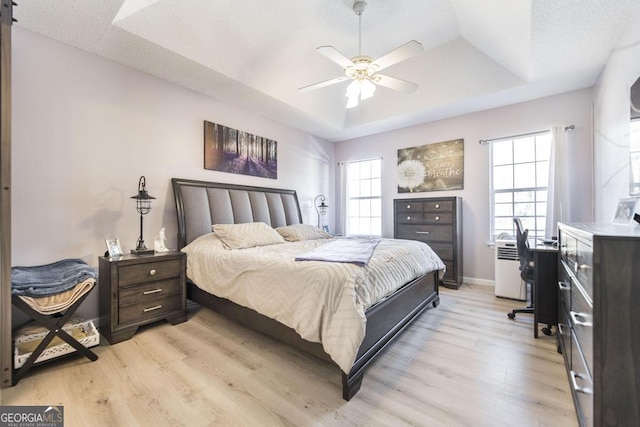 bedroom featuring light hardwood / wood-style flooring, ceiling fan, and a tray ceiling