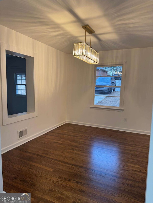 spare room featuring dark wood-type flooring and a notable chandelier