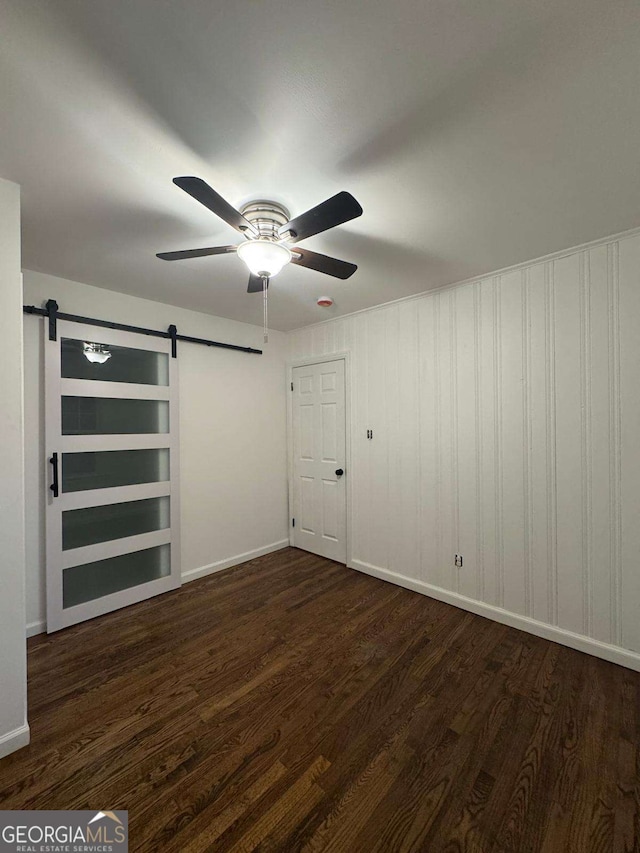 spare room featuring dark wood-type flooring, a barn door, and ceiling fan