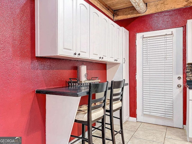 kitchen featuring a kitchen bar, wood ceiling, light tile patterned floors, beamed ceiling, and white cabinets