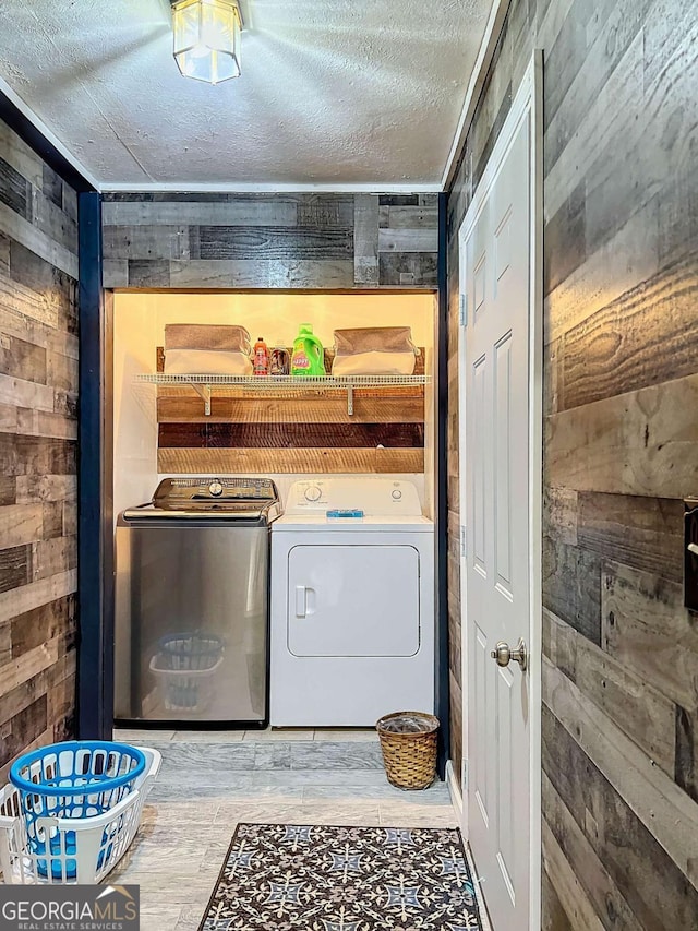 washroom with washer and dryer, a textured ceiling, and wooden walls