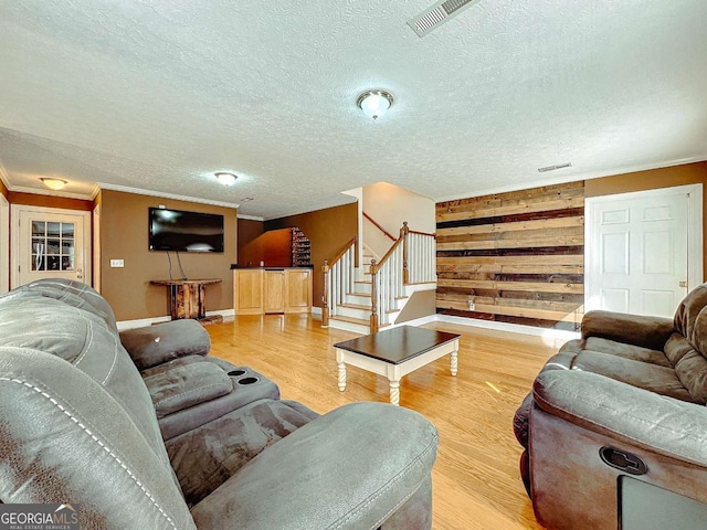 living room featuring crown molding, light hardwood / wood-style floors, a textured ceiling, and wood walls