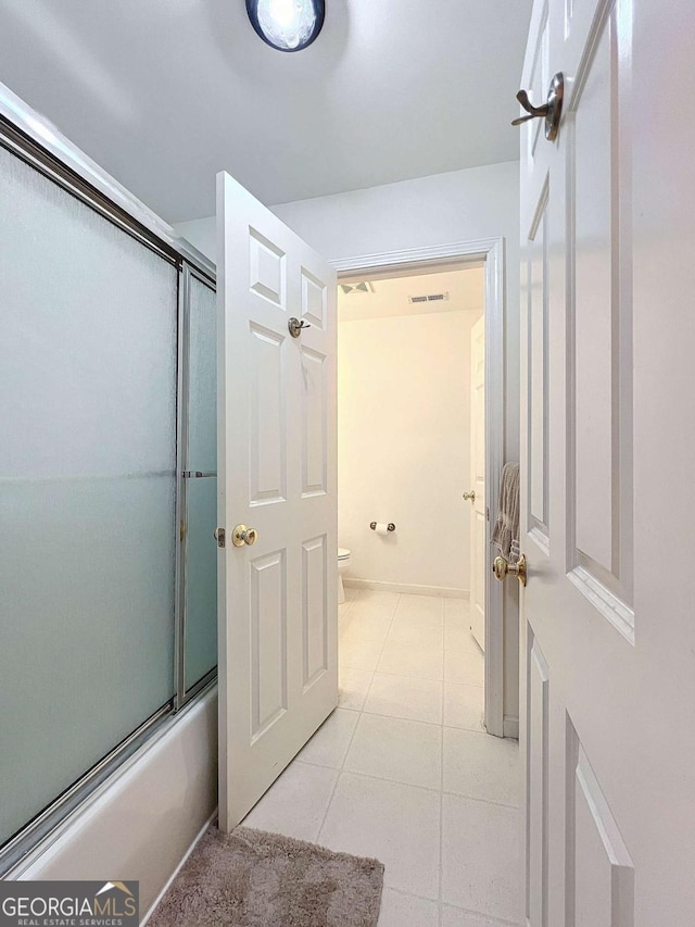 bathroom with tile patterned flooring, combined bath / shower with glass door, and toilet