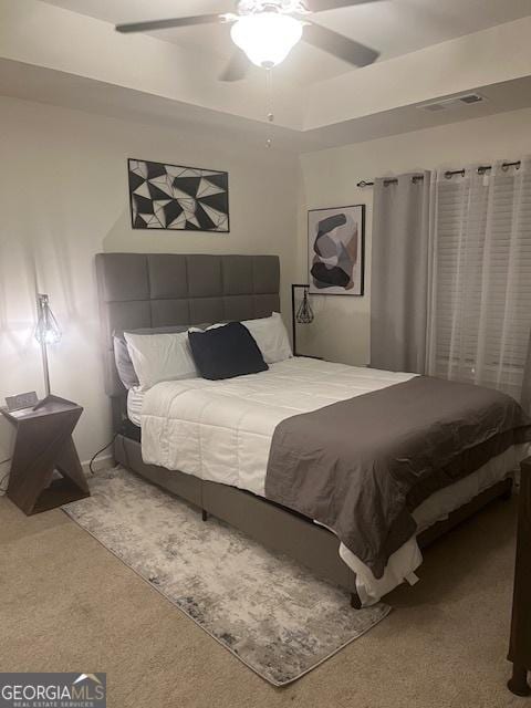 bedroom featuring a raised ceiling, ceiling fan, and carpet