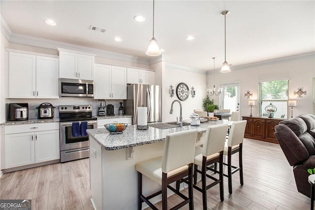 kitchen with stainless steel appliances, white cabinetry, a center island with sink, and pendant lighting