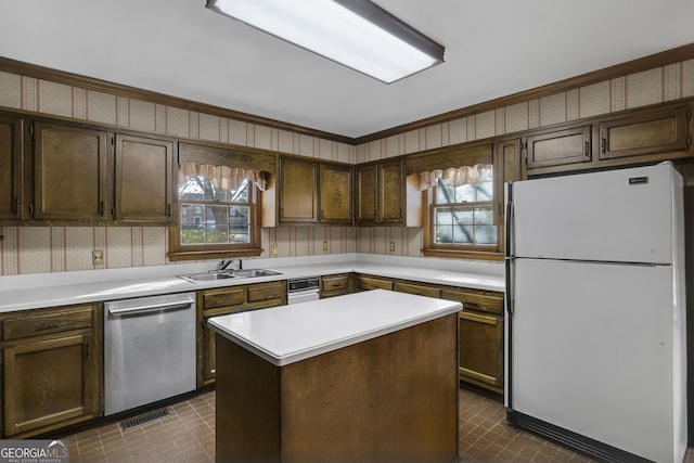 kitchen with a center island, light countertops, stainless steel dishwasher, freestanding refrigerator, and wallpapered walls