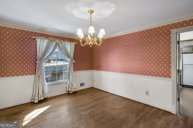 unfurnished dining area featuring wallpapered walls, crown molding, wood finished floors, and wainscoting