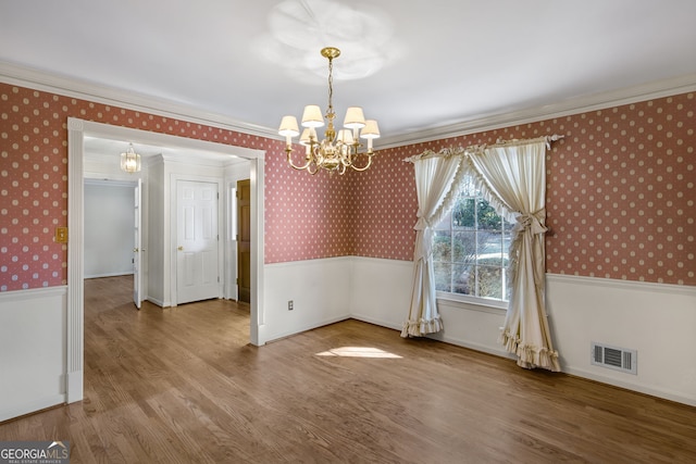 unfurnished dining area with wallpapered walls, visible vents, a wainscoted wall, and wood finished floors